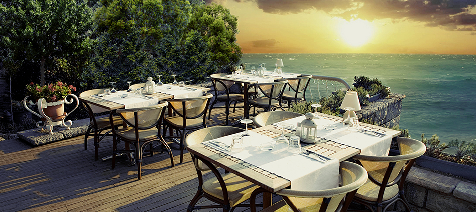 Dining tables outside on patio overlooking the ocean at sunset