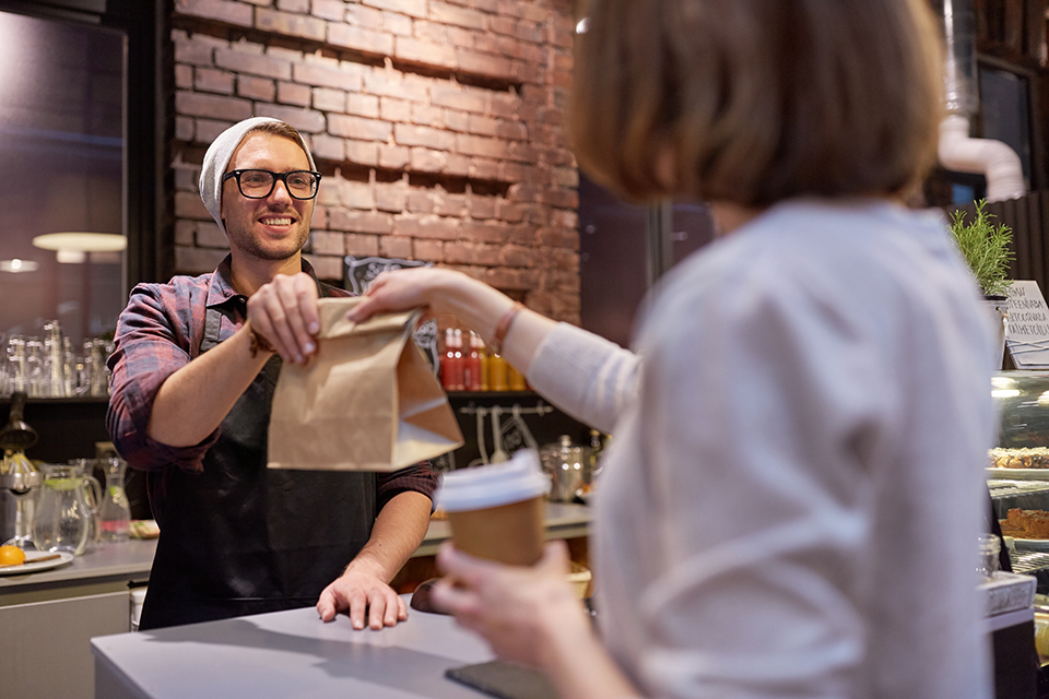 Male coffee shop employee hands female customer their takeout order