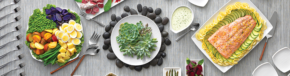 White plates, platters, and stainless-steel utensils with food and succulents displayed on table