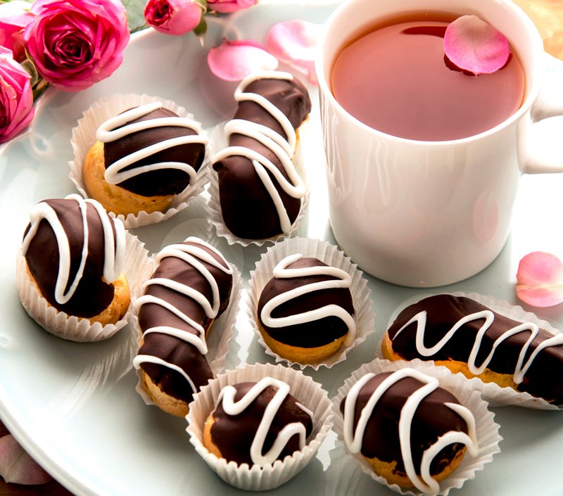 Mini Éclair pastries on plate with tea in mug and roses
