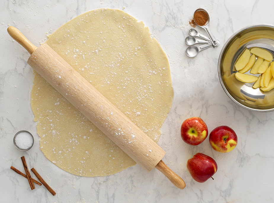 Dough with Culinary Essentials rolling pin and measuring spoons with apples on table
