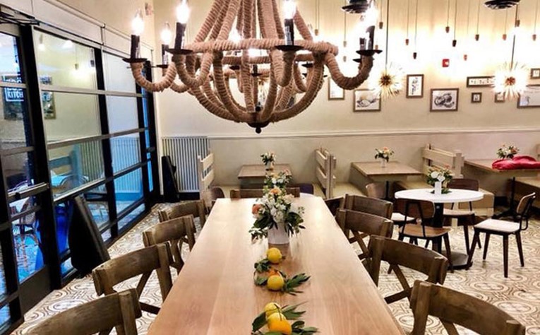 Interior at Zoës Kitchen, Family-style wood table with decorative flowers, fruit, and lighting fixture hanging overhead