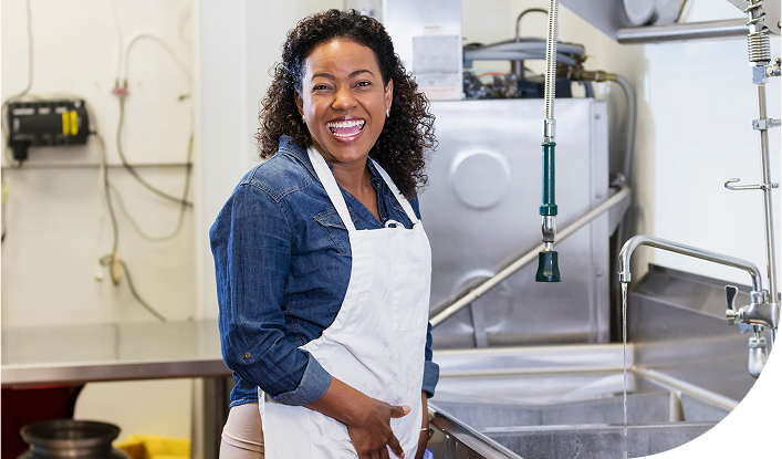 Employee smiling and cleaning dishes in an industrail kitchen